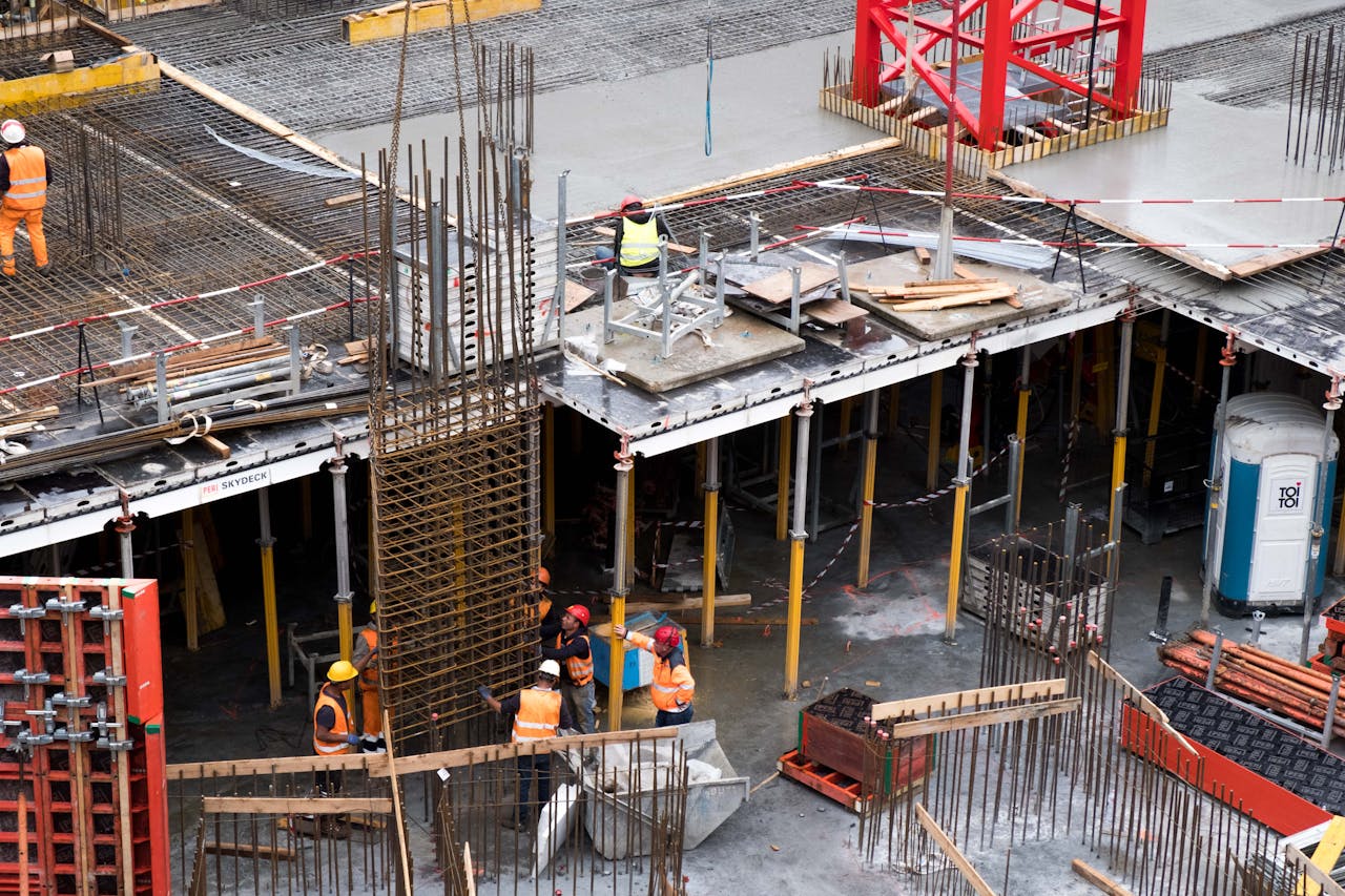 services-01 Workers in high visibility gear at a busy construction site with scaffolding and steel frames.