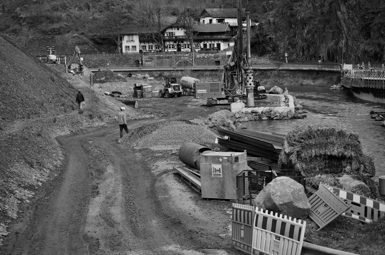 about-04 Monochrome image of construction site next to a river with heavy machinery and workers.